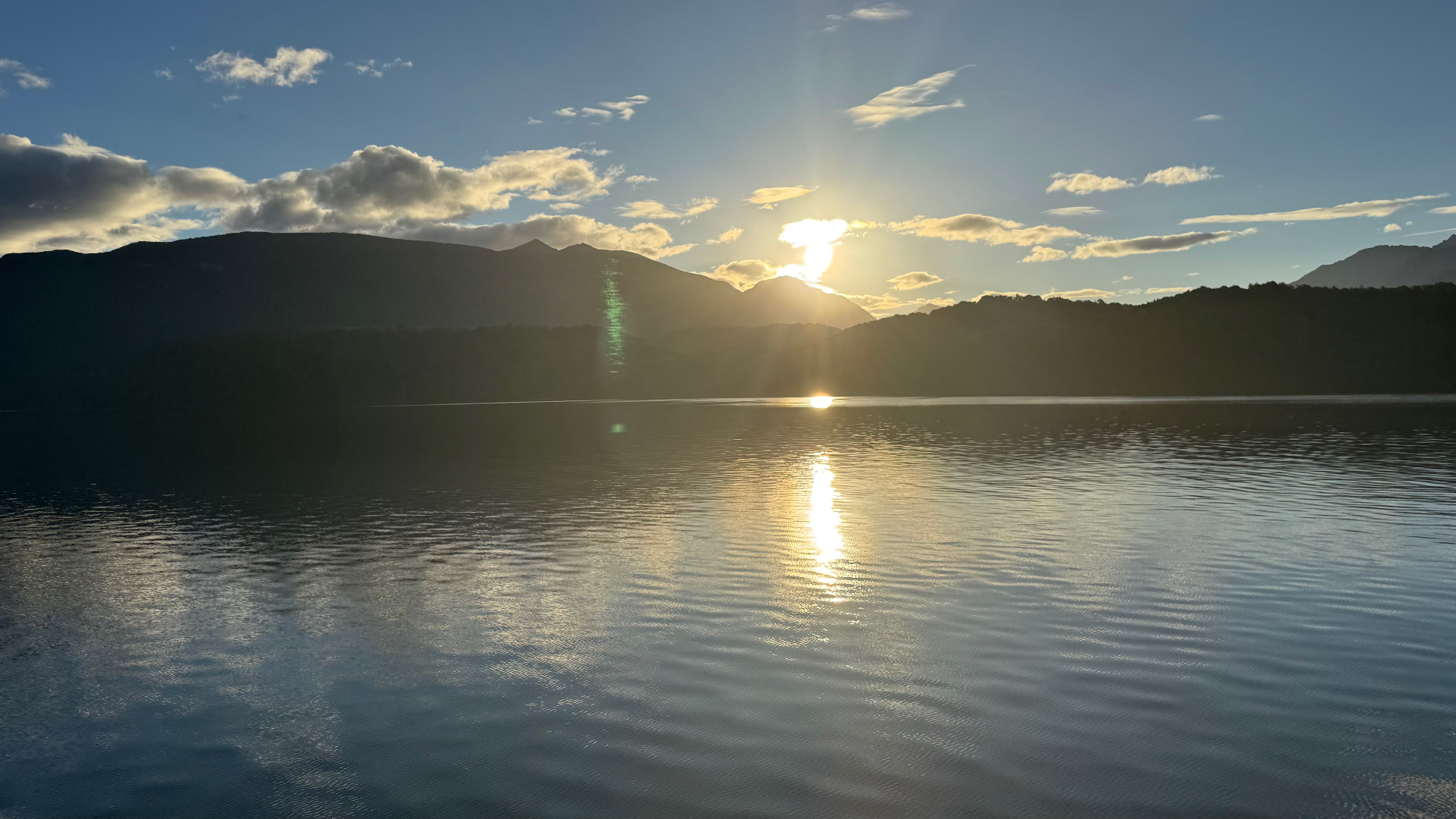 The sun setting behind hills, reflected in the still water of Lake Te Anau