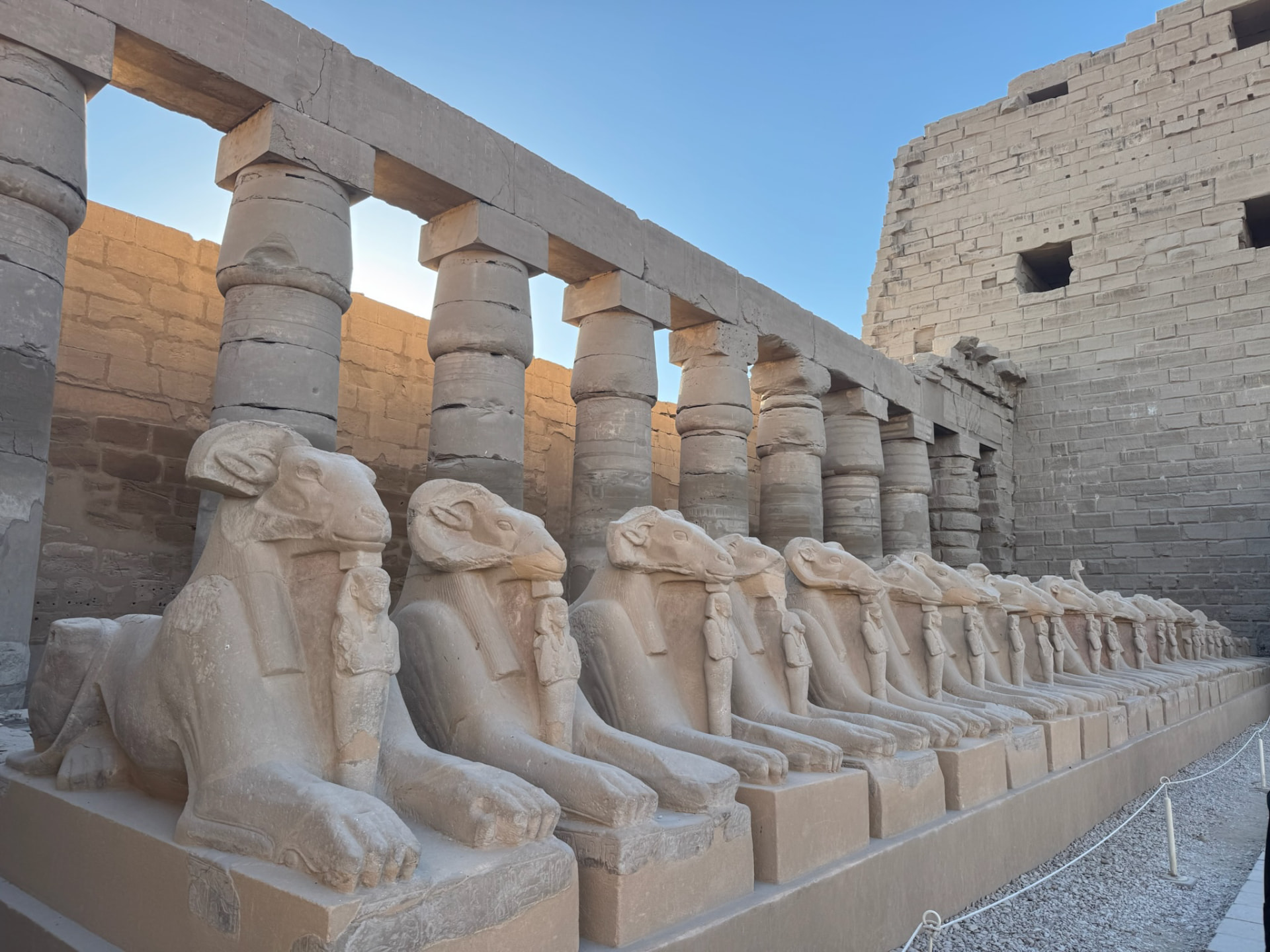 A row of ram-headed sphinxes along the approach to Karnak with columns behind
