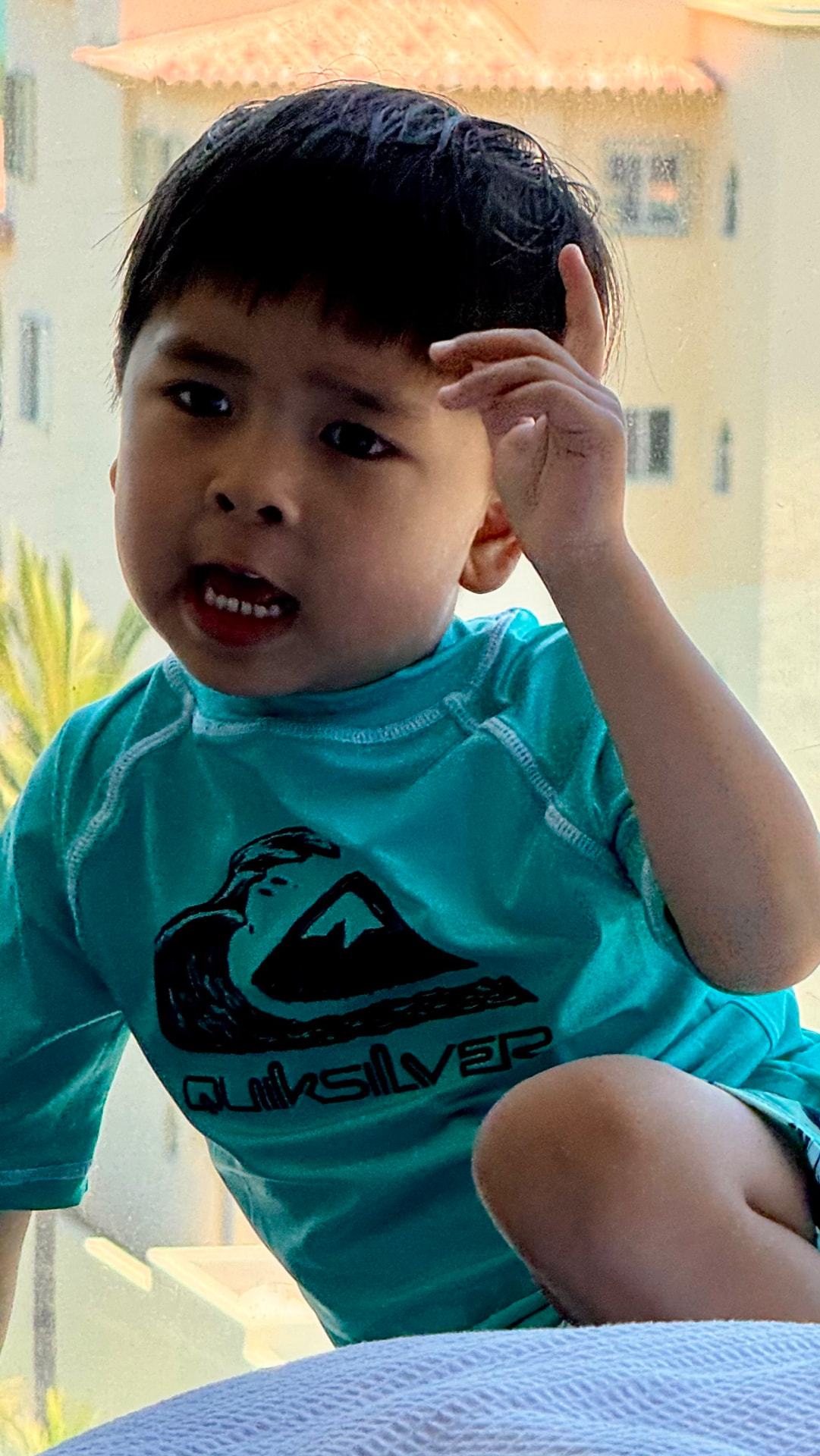 A young boy in a turquoise rash guard sitting by a bright window