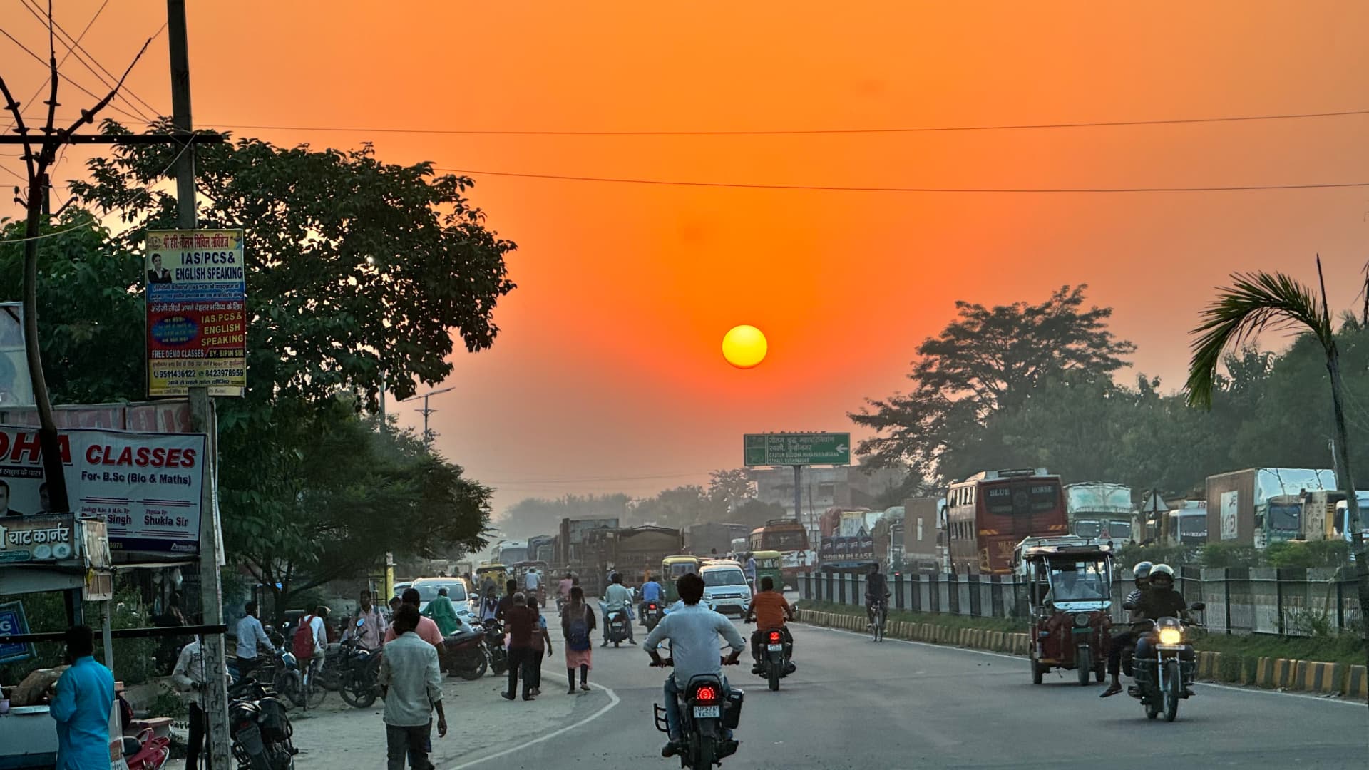 An orange sun hangs low above a busy road. — Kushinagar, Uttar Pradesh, India.