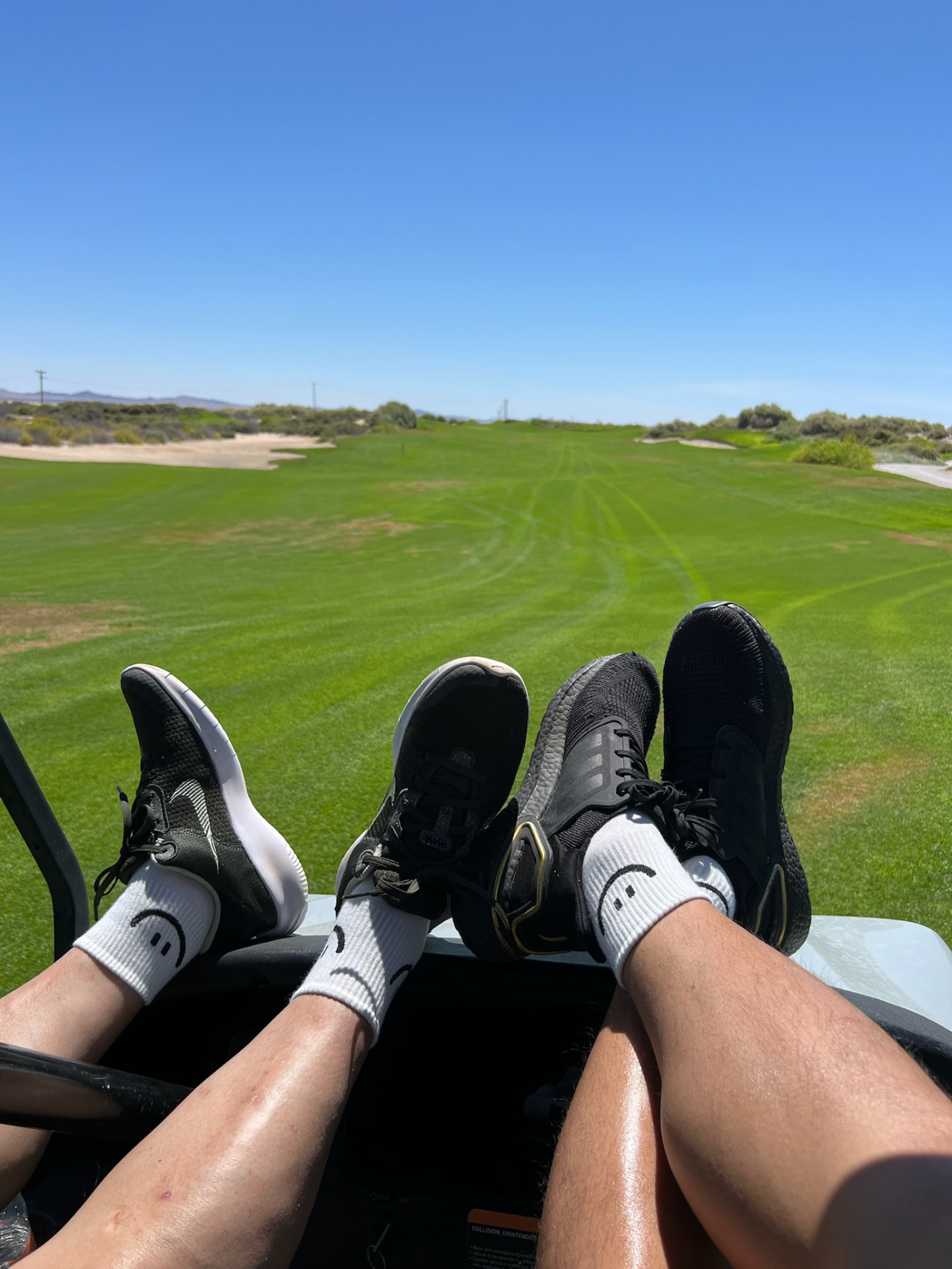 Two golfers resting their feet in a cart beside a green fairway