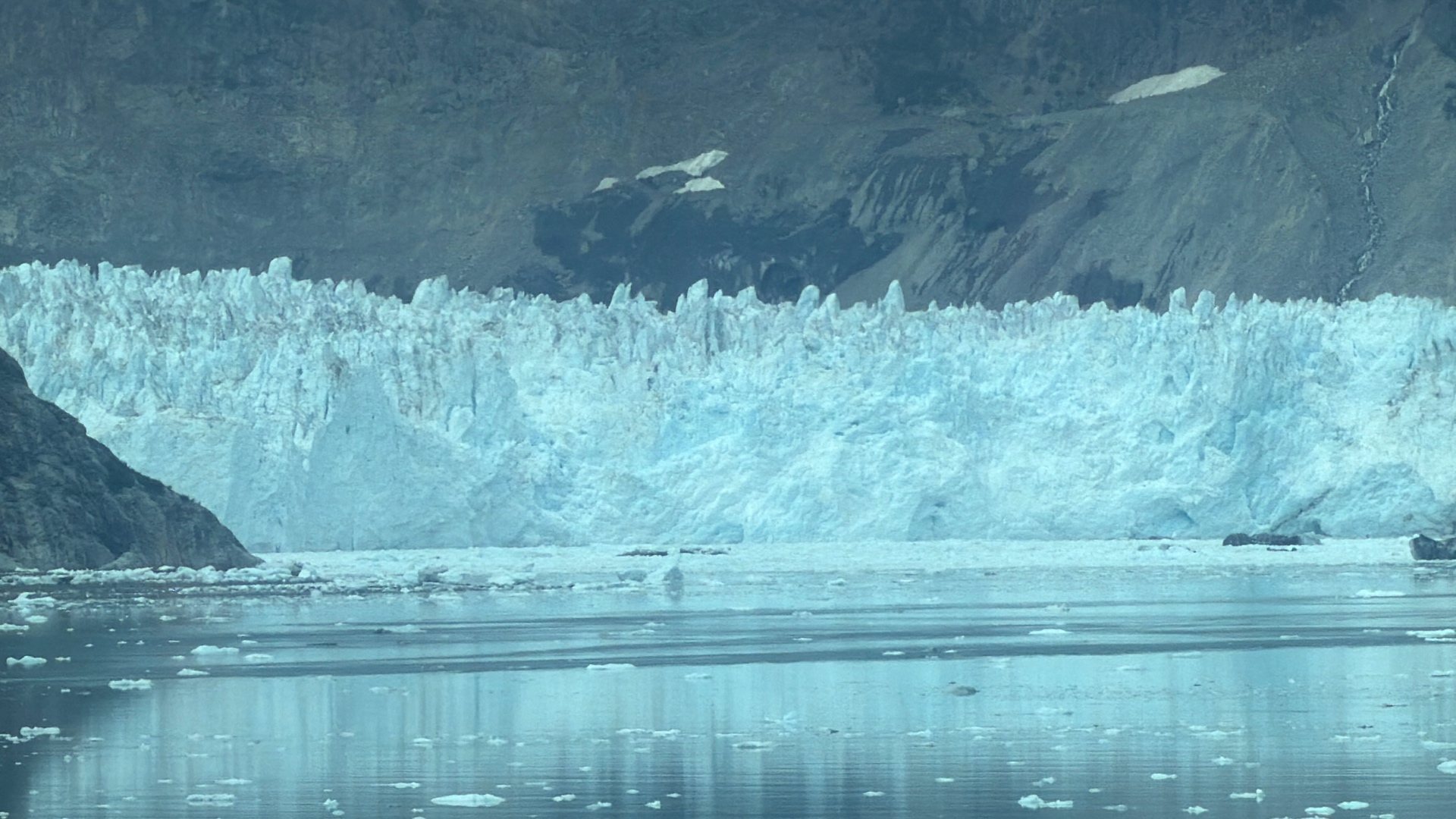 Close view of the jagged blue face of a tidewater glacier reflected in calm water