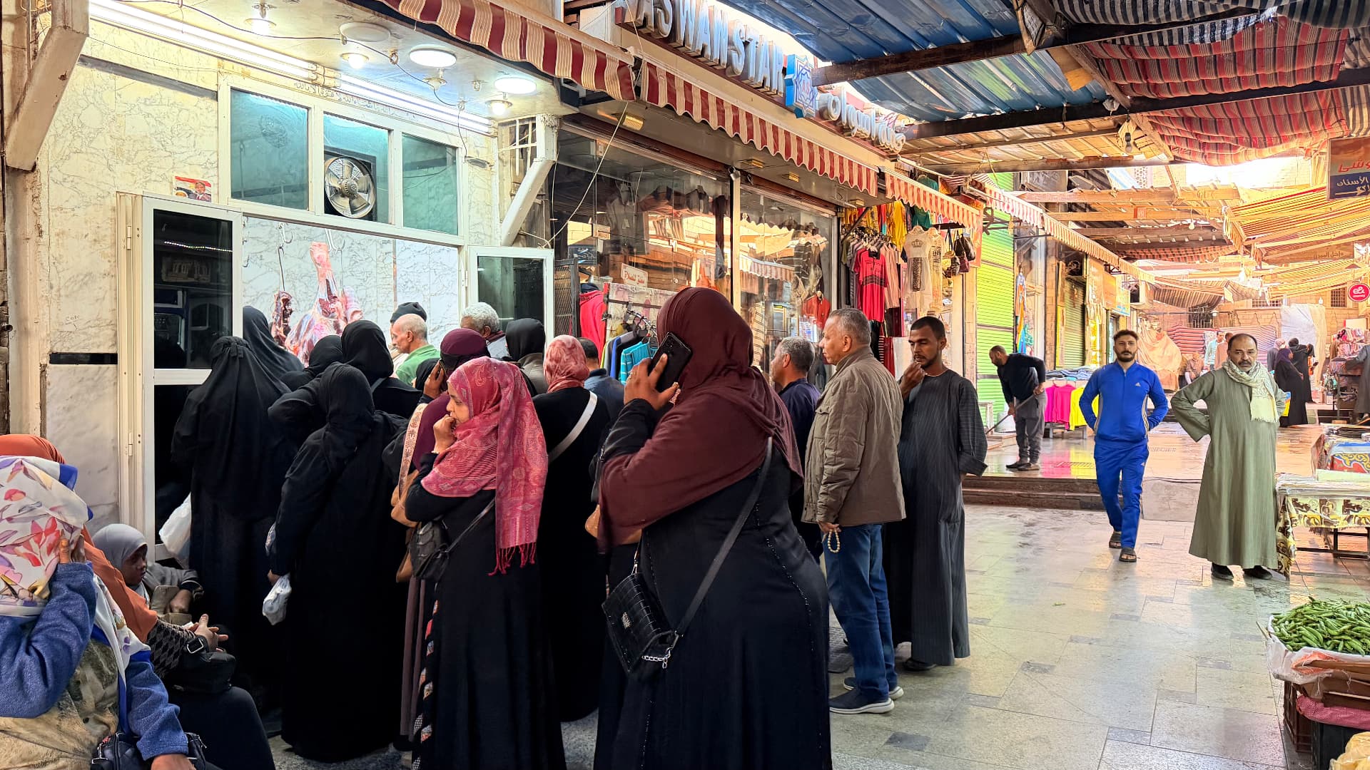 A crowded market street in Aswan with shoppers gathered outside a butcher's shop