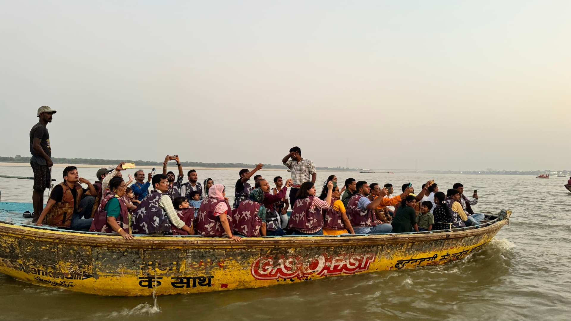 A boat full of passengers passes along the Ganges. — Varanasi, Uttar Pradesh, India.