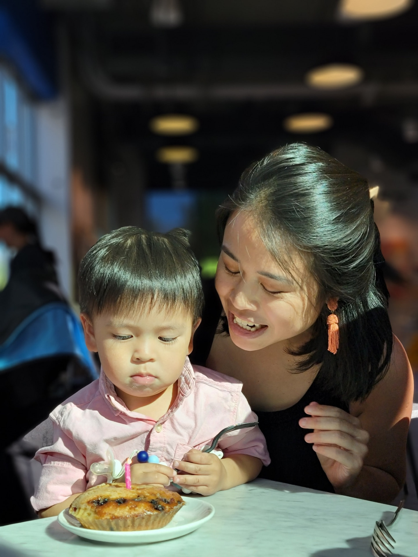 A mother smiling at her son as he sits with a birthday pastry at a café