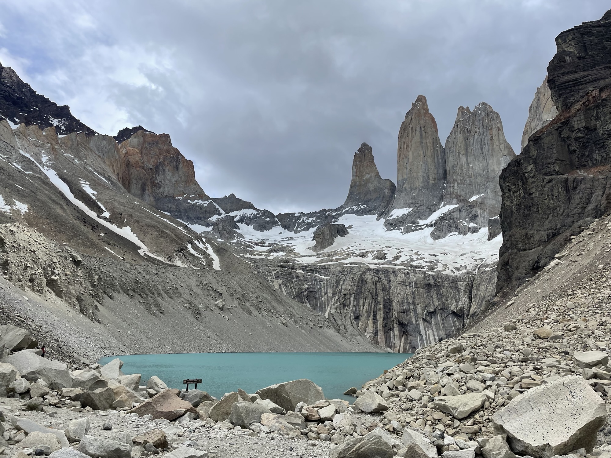 The three granite towers of Torres del Paine rising above a turquoise glacial lake ringed by boulders and snow