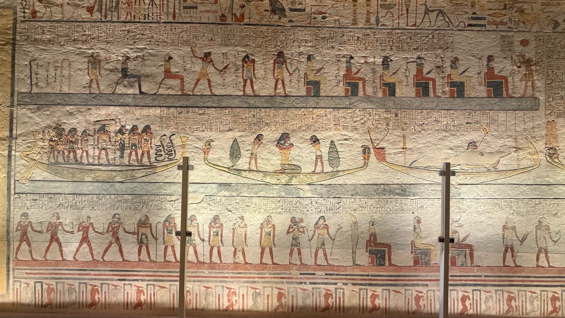 A painted tomb wall showing rows of figures and solar barques in red, yellow and black