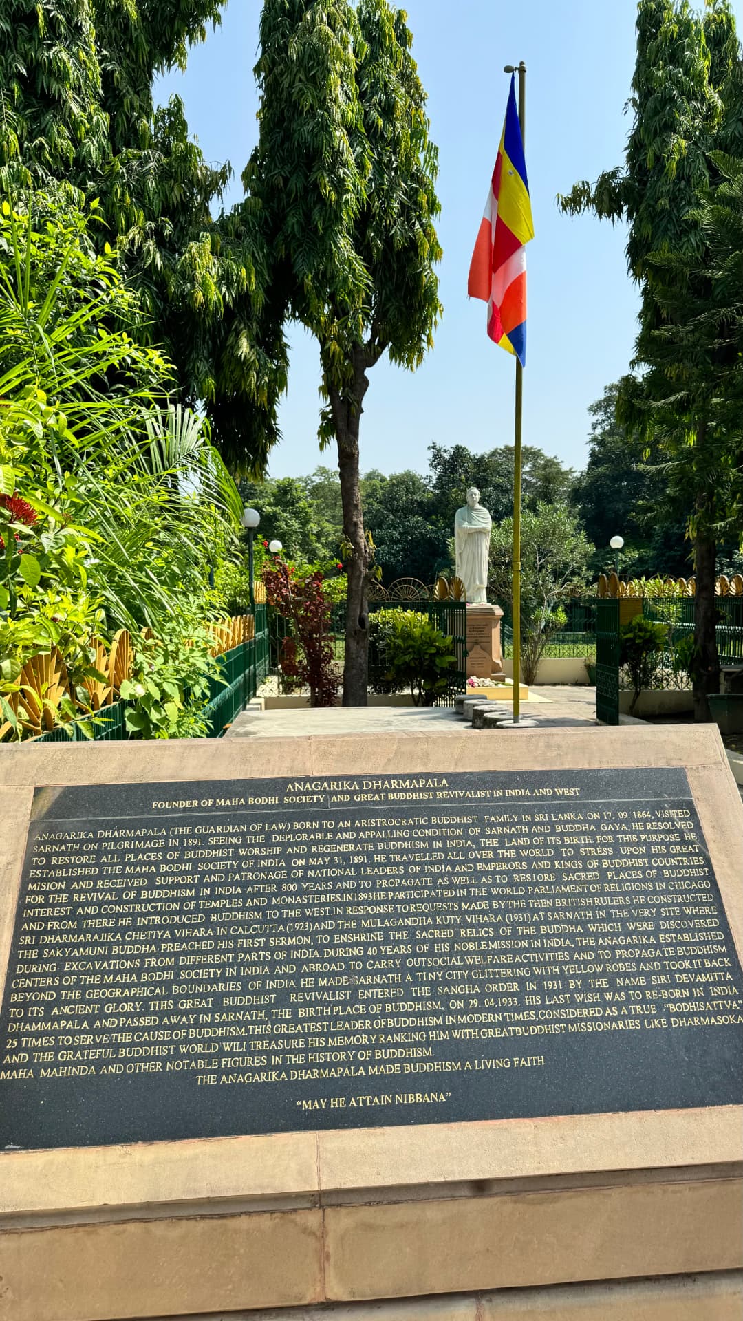 A Buddhist memorial in the garden, with flags and tall trees behind it. — Sarnath, Uttar Pradesh, India.