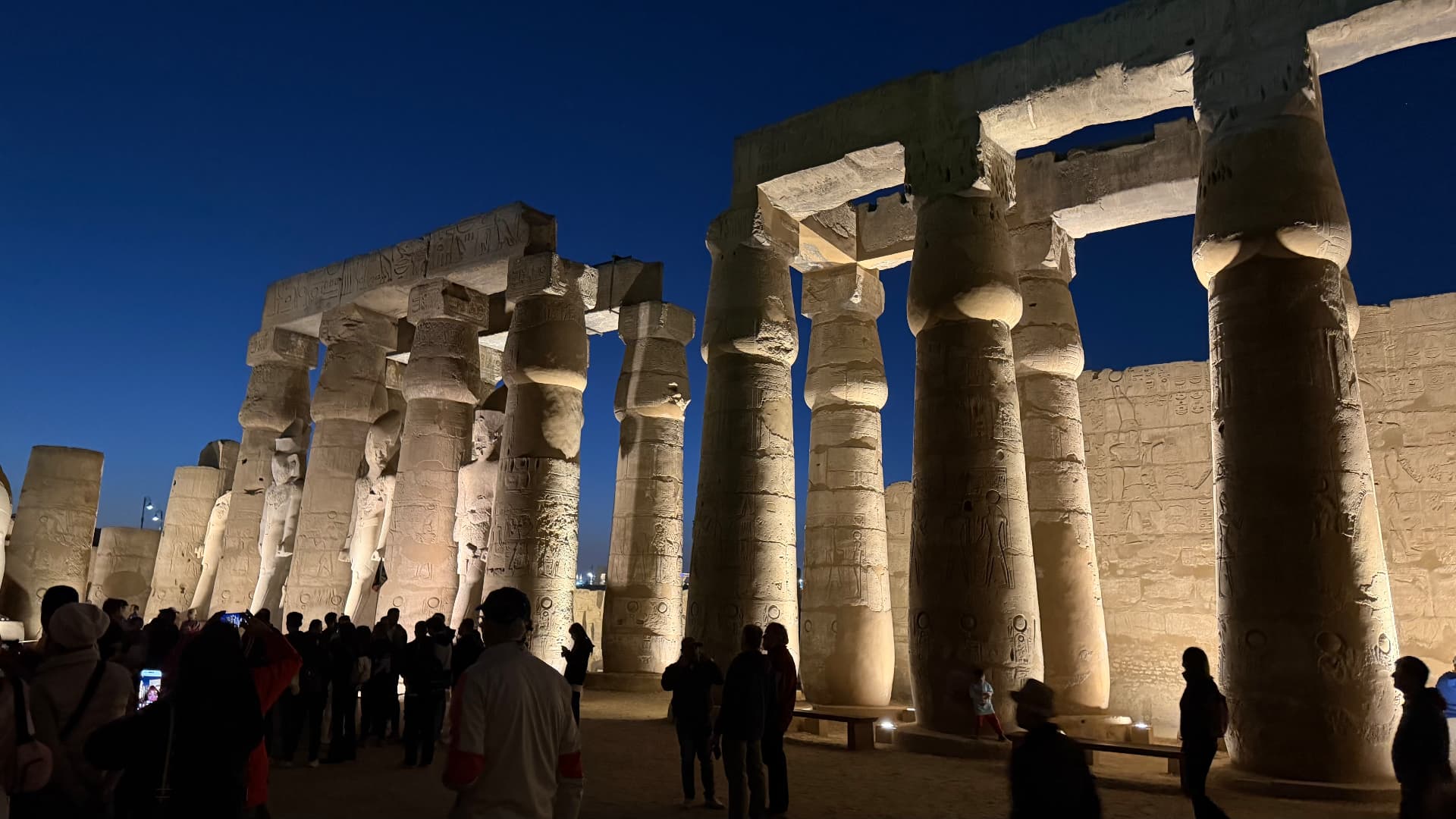 The colonnade of Luxor Temple lit at night with visitors walking among the columns