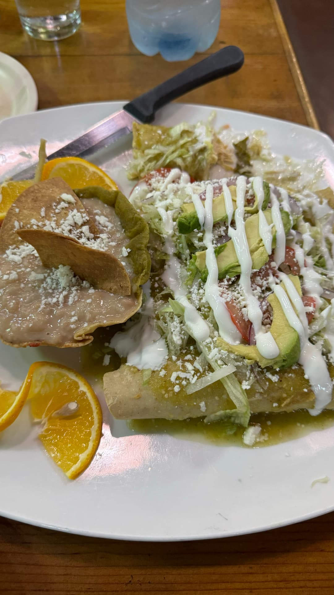 A plate of enchiladas with avocado, refried beans, and orange slices