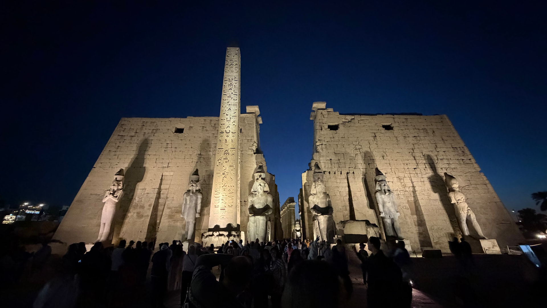 The pylon of Luxor Temple at night with statues of Ramesses and the obelisk lit from below