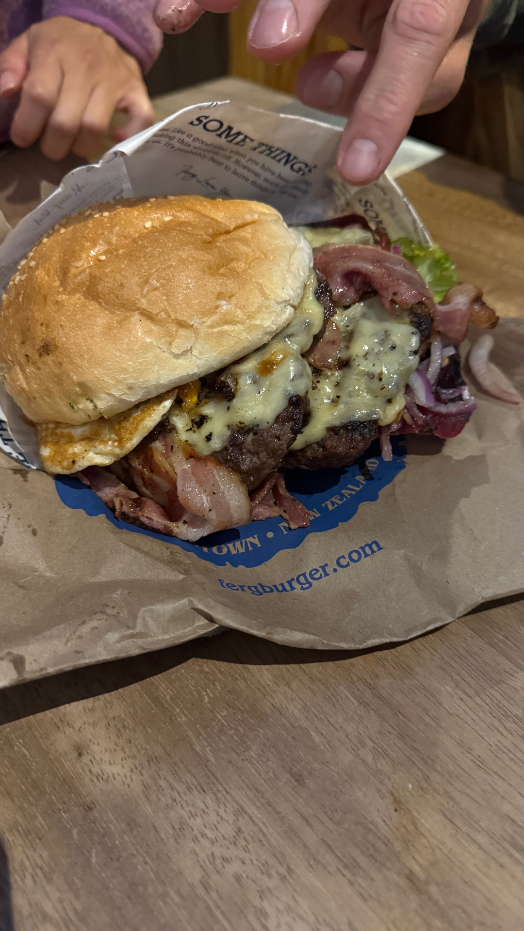 A stacked beef burger with cheese, bacon, egg, lettuce, and onion on a wooden table