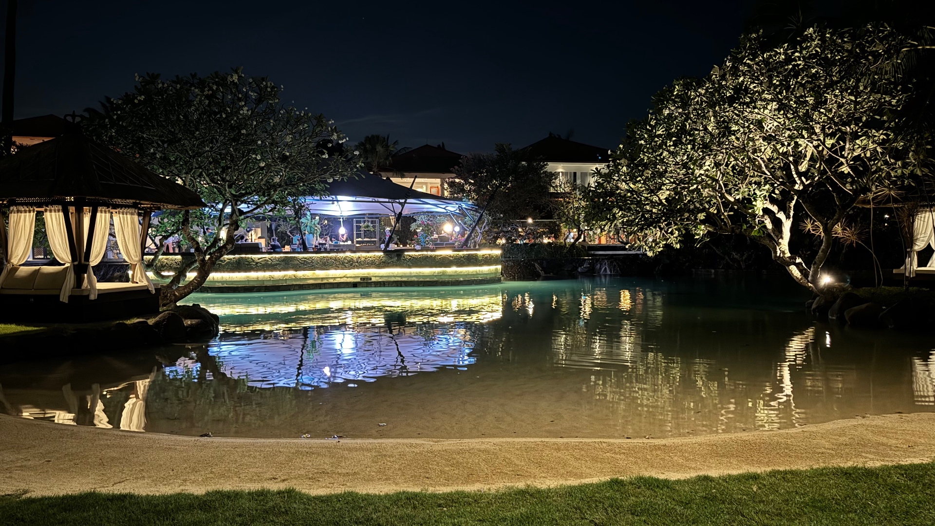 Lagoon pool reflecting an illuminated floating stage and garden cabanas