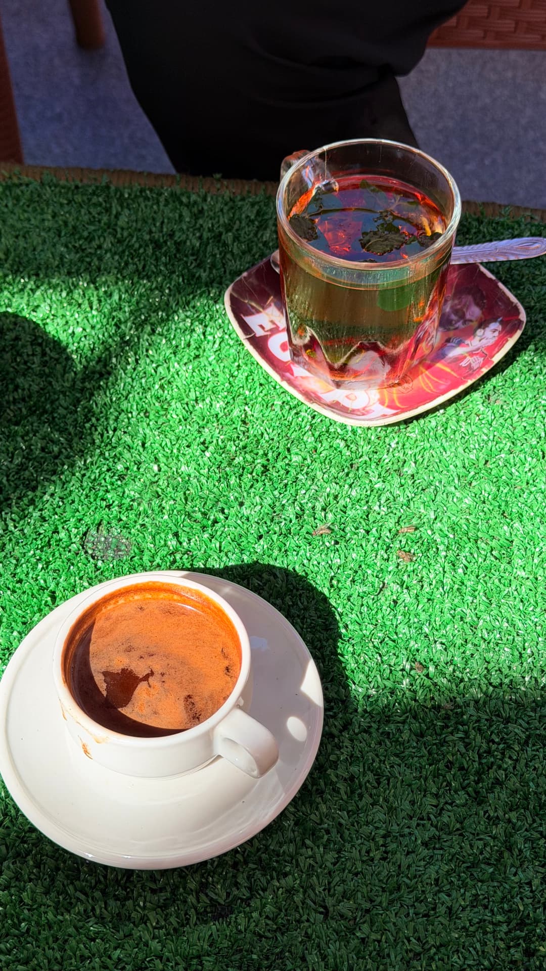 A glass of mint tea and a cup of Egyptian coffee on a green table