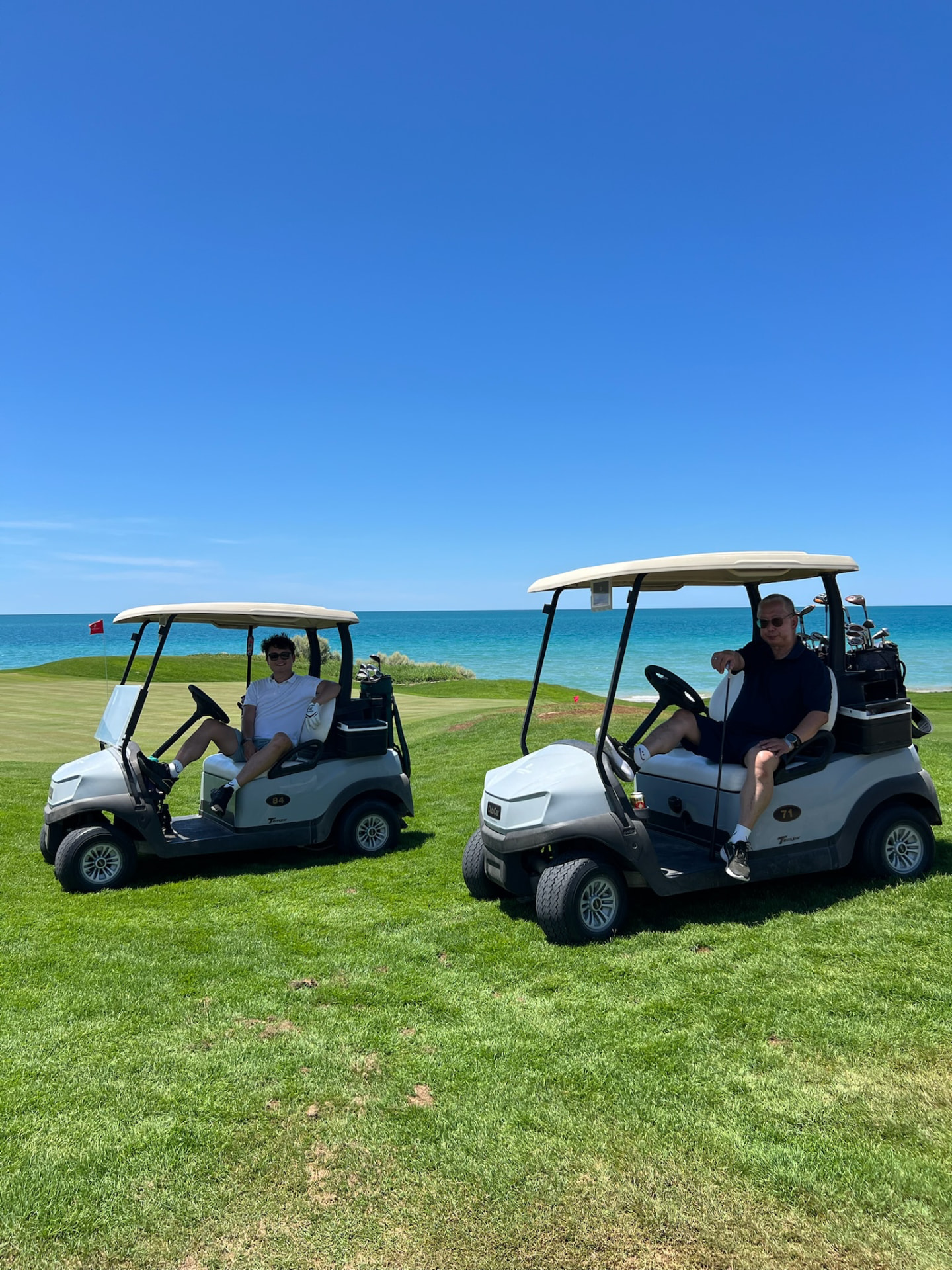 Ken and Johan seated in golf carts on an oceanfront course