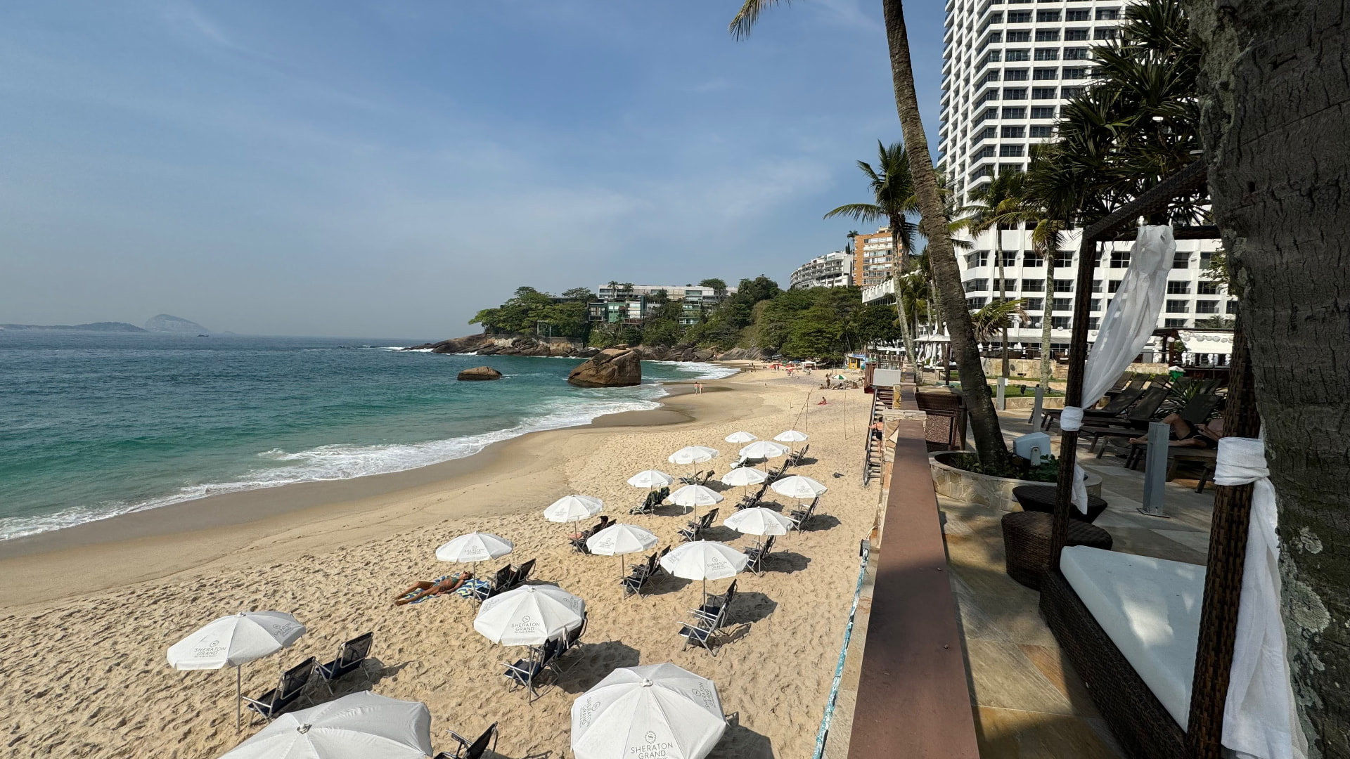 White Sheraton beach umbrellas and loungers on the sand beside a turquoise cove