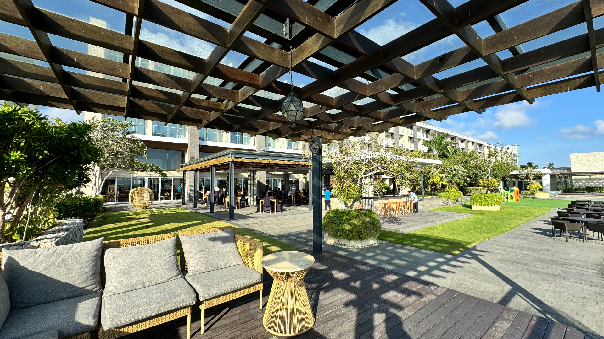 Open-air terrace with a timber pergola, lawn and the resort building beyond
