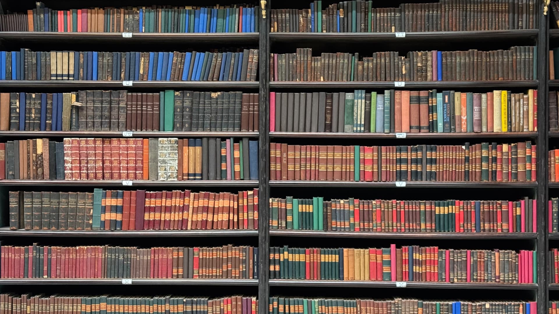 Closely packed historic books arranged across dark wooden shelves