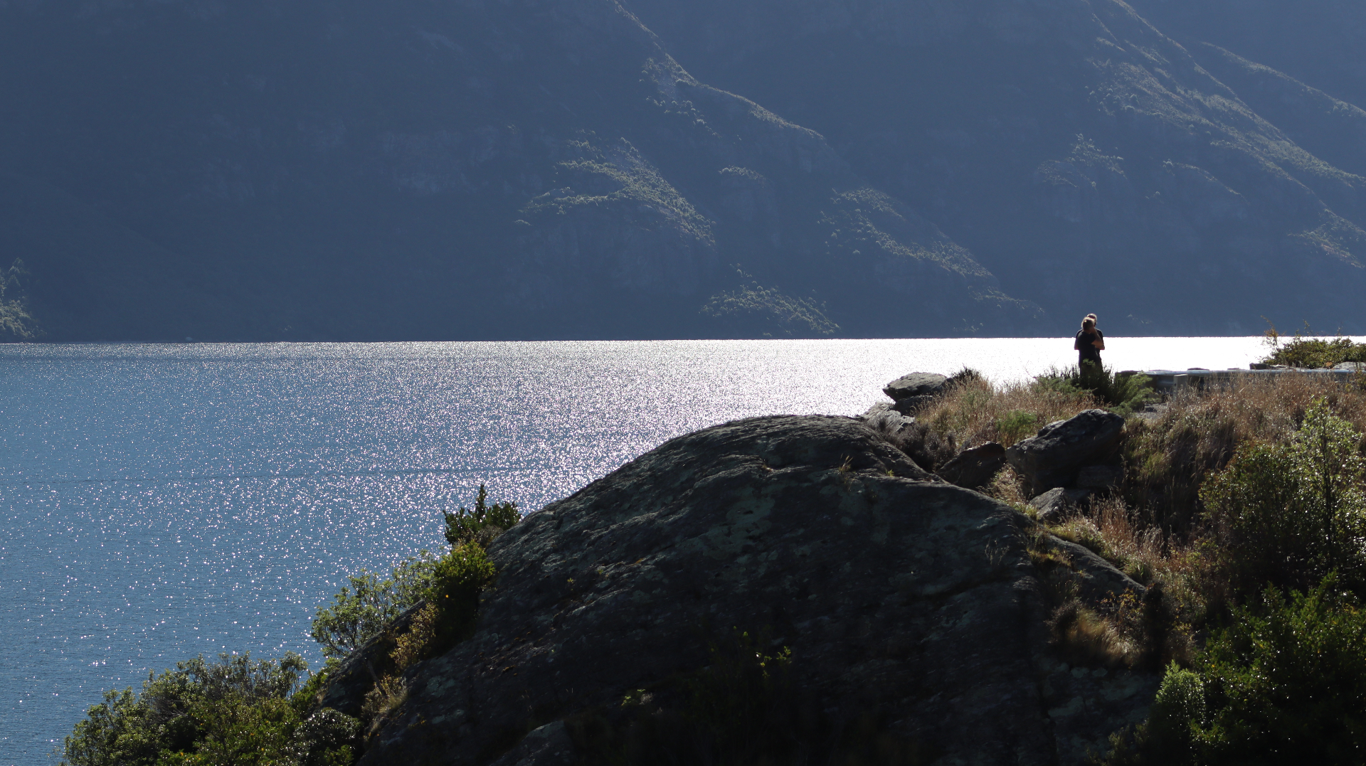 Silver light on a lake below a steep dark mountainside