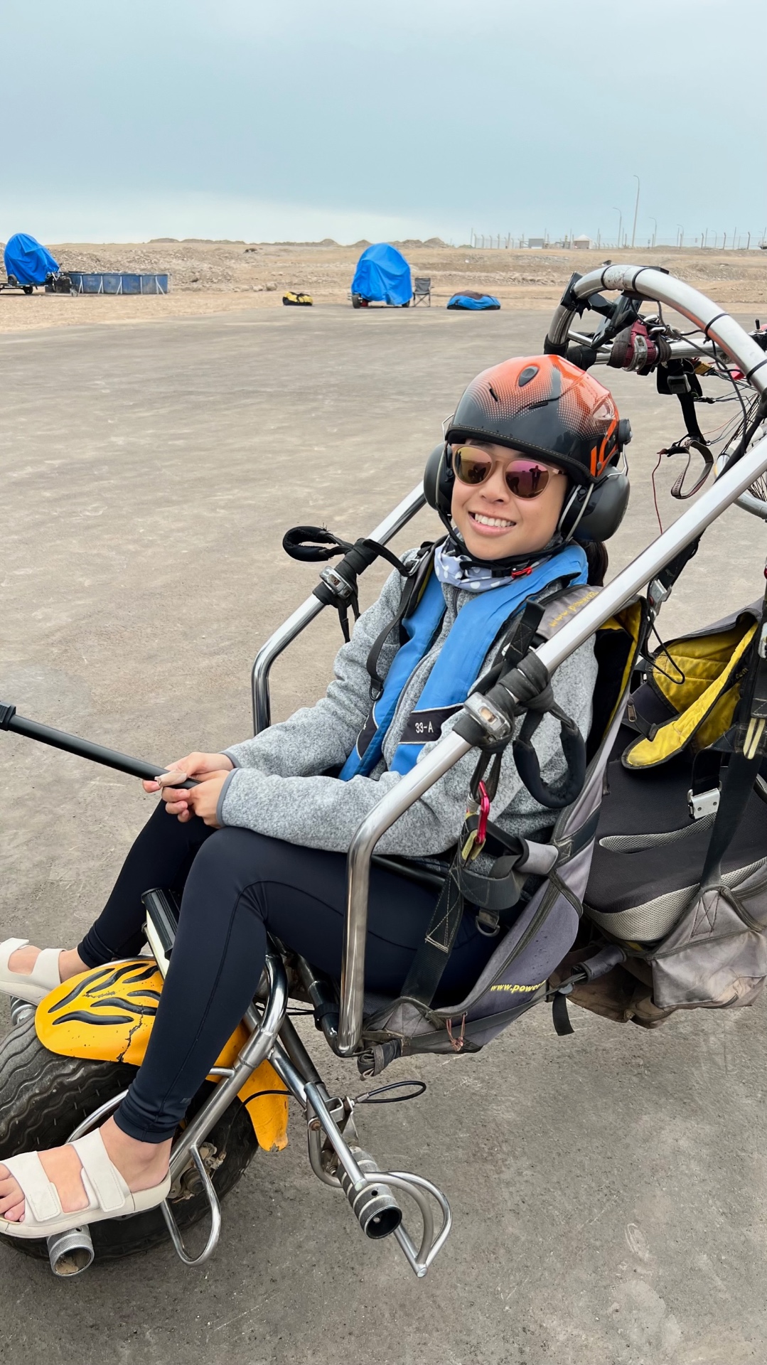 Smiling woman seated in a powered paragliding trike wearing a helmet and harness