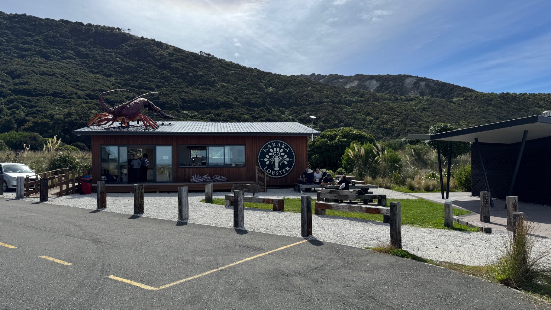 The Karaka Lobster shop, a timber building with a giant crayfish sculpture on the roof, backed by green hills