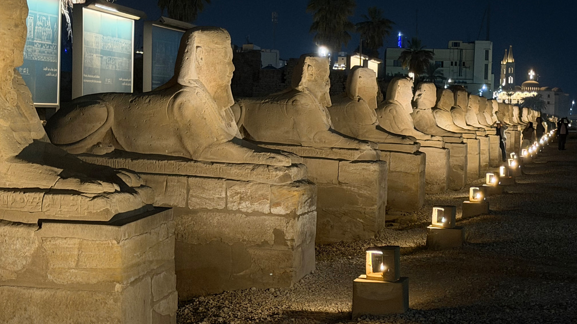 The Avenue of the Sphinxes at night, lit by a lamp at every plinth, running toward the town