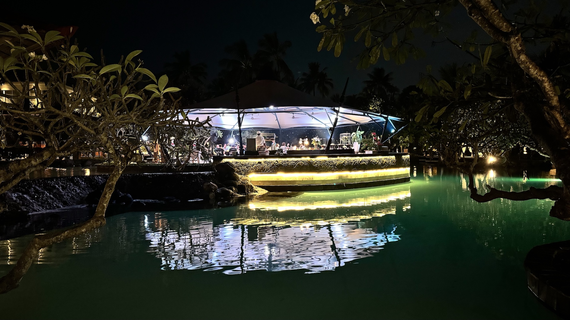 Floating stage glowing across the dark lagoon among tropical trees