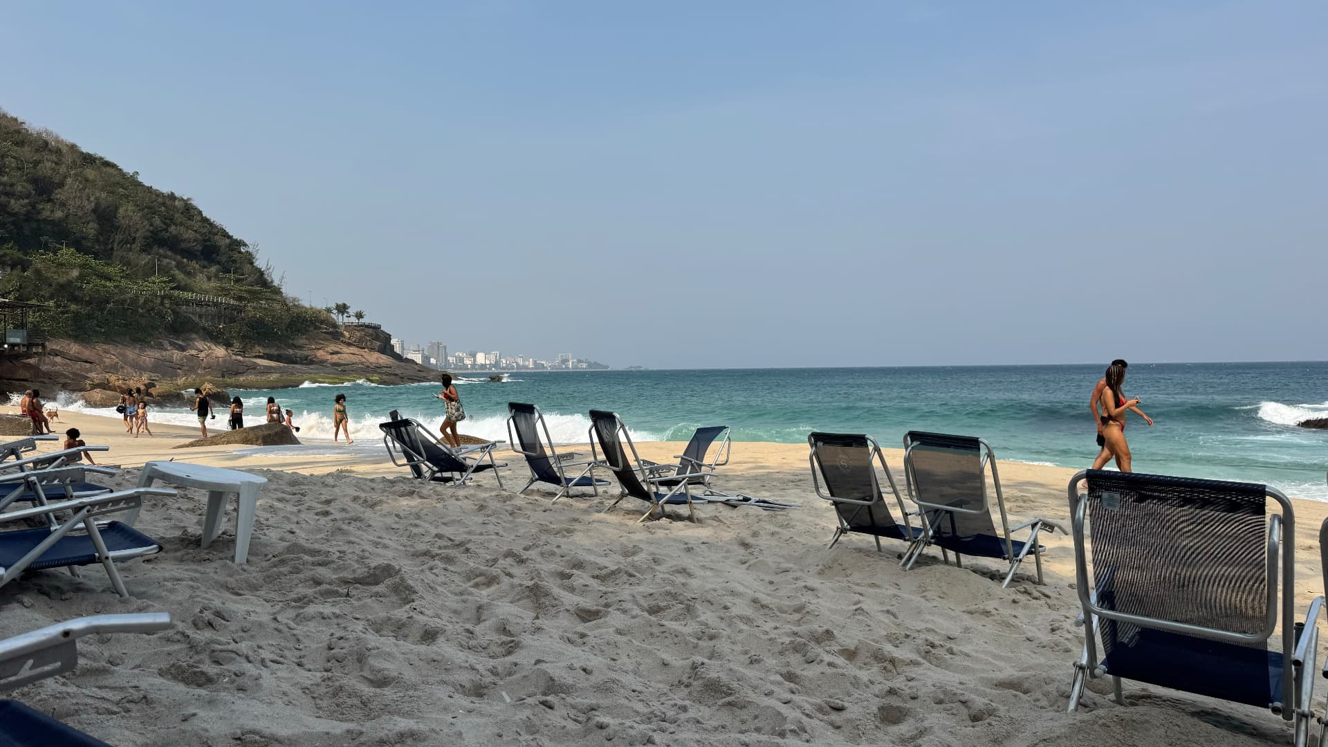 Empty beach chairs on the sand with swimmers and the city skyline in the distance