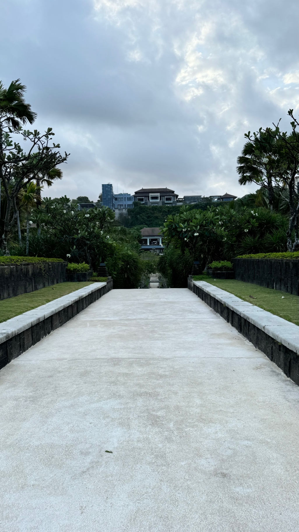 Broad resort path framed by tropical gardens beneath a cloudy sky