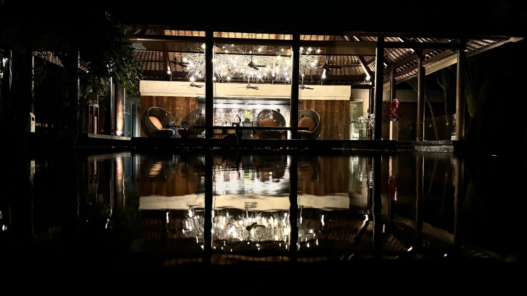 Lit lounge pavilion mirrored in still dark water at night