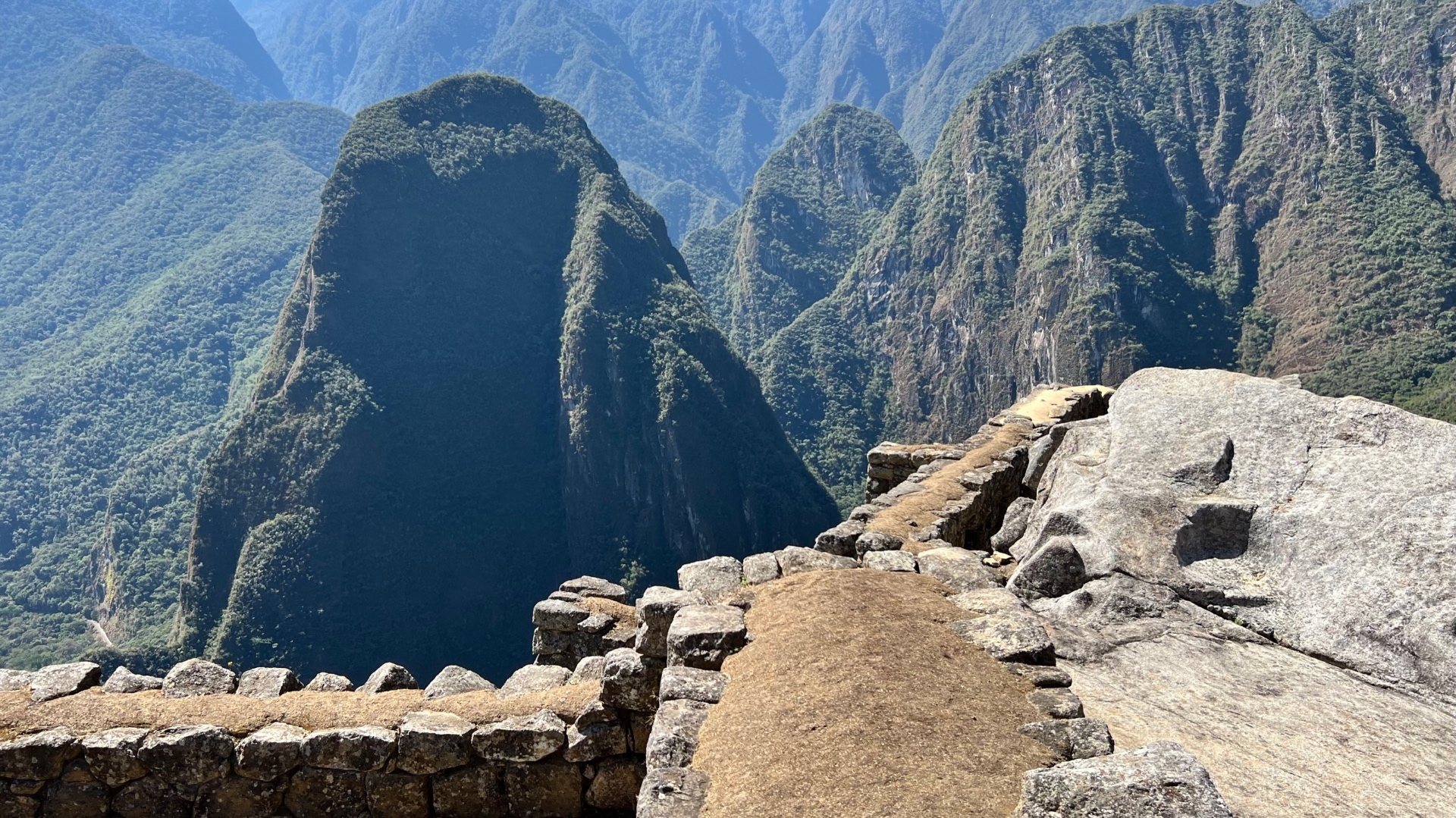 Carved stone platform at the edge of Machu Picchu overlooking rounded green peaks