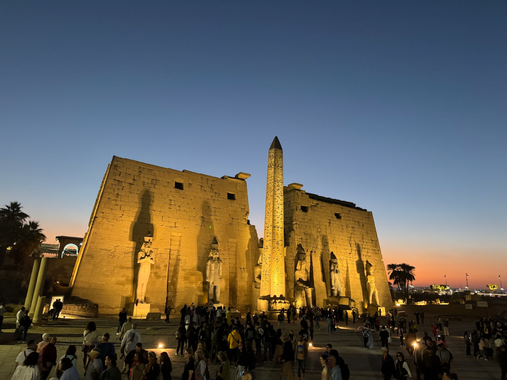 Luxor Temple floodlit at dusk with its obelisk and seated colossi, an orange sky behind