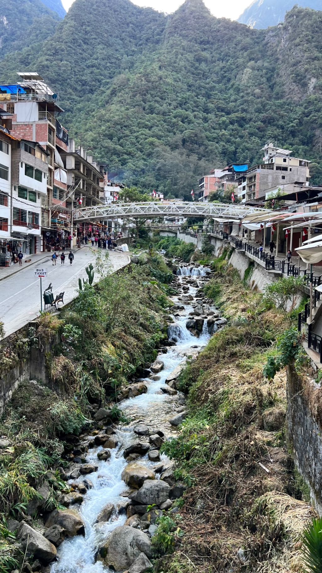 Aguas Calientes with a rocky stream running between buildings beneath forested mountains