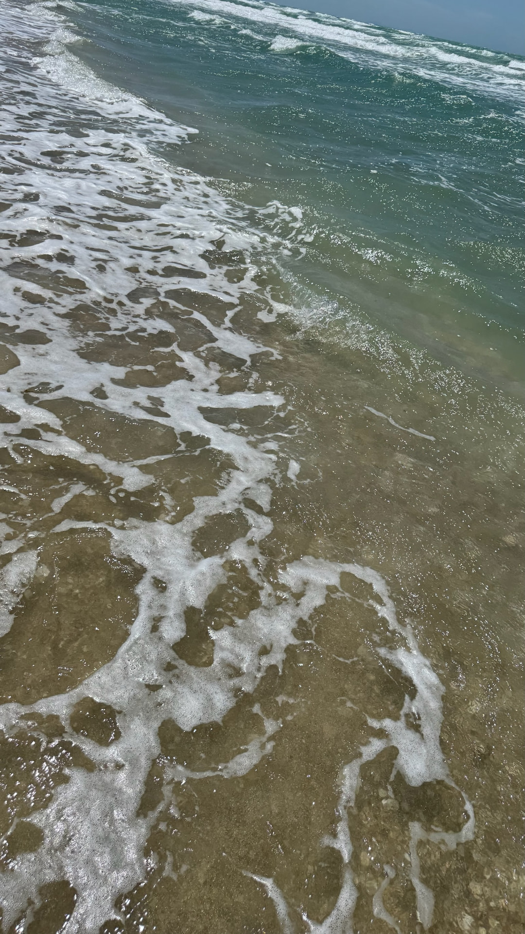 Clear green-blue water washing over wet sand