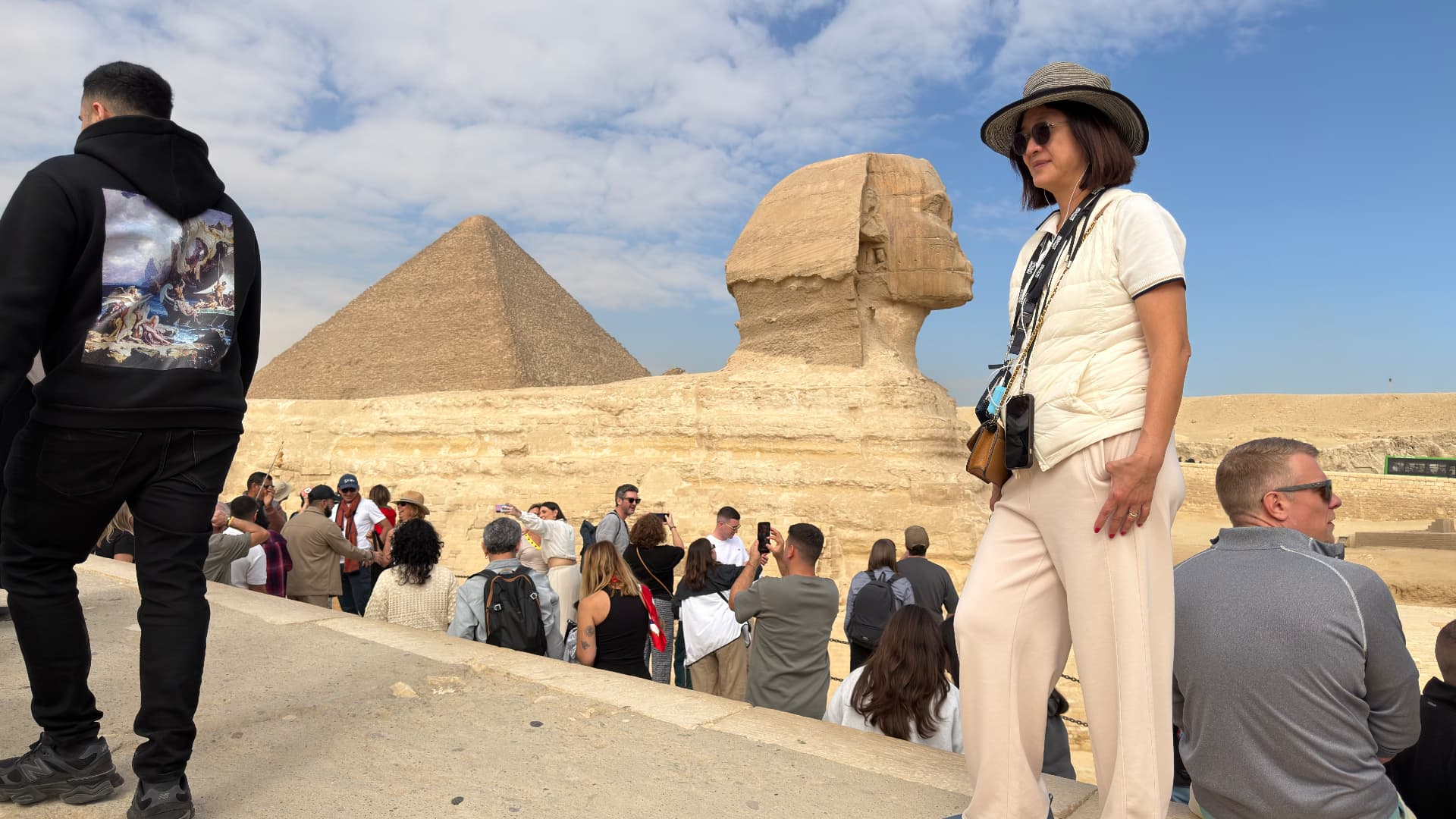 The Great Sphinx with a pyramid behind it and a crowd of visitors along the viewing wall