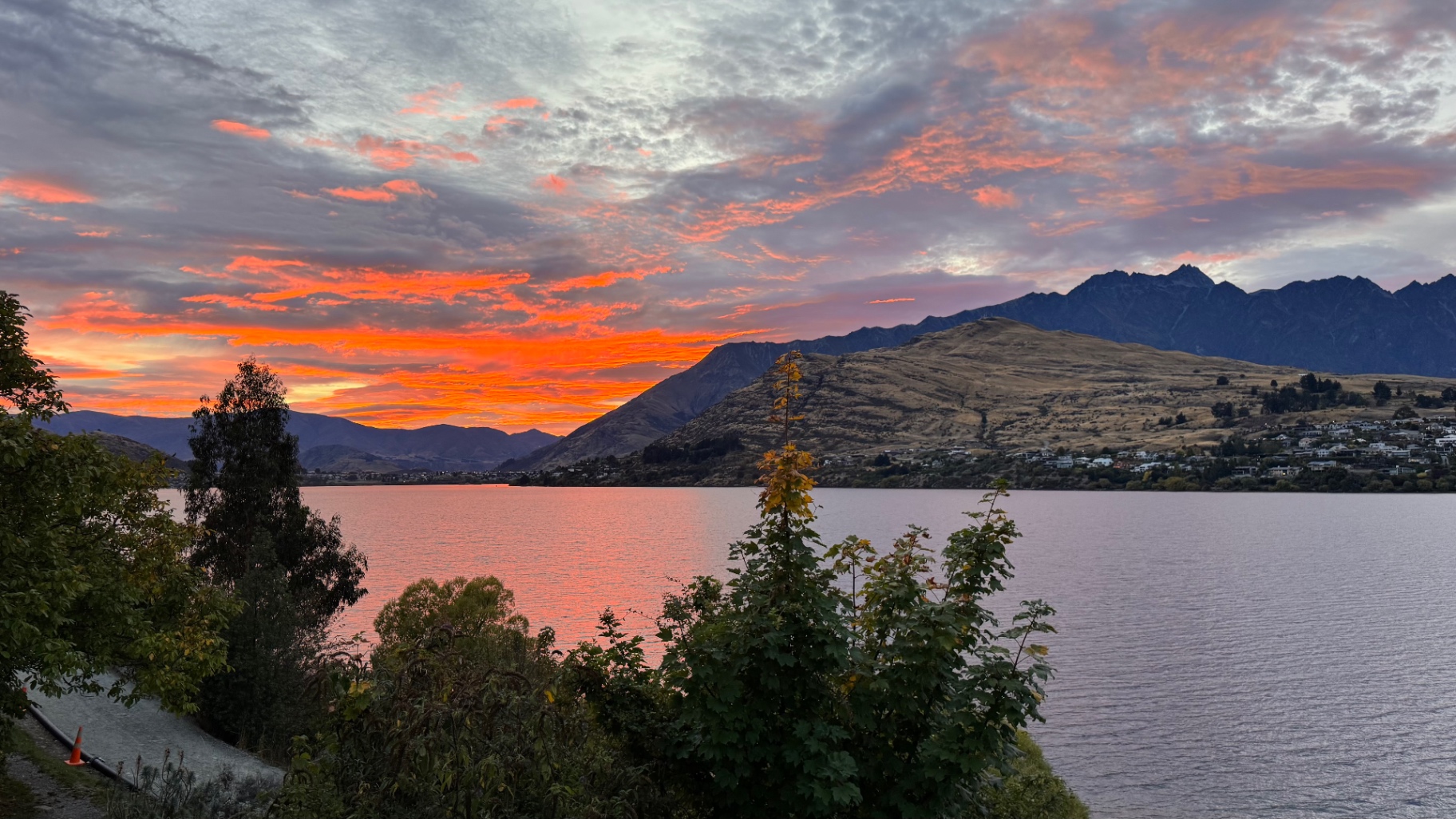 A lake at dawn with fiery orange and pink streaks across the sky, reflected in the water below dark mountains
