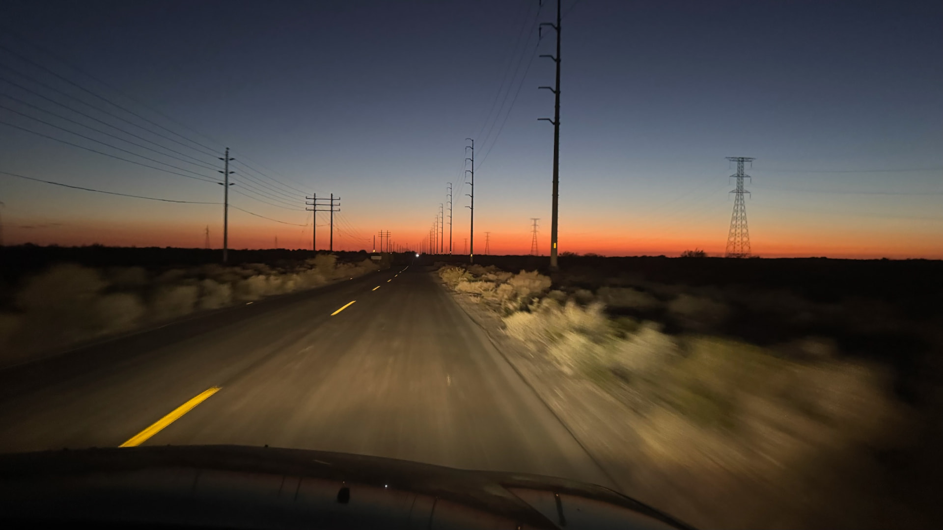 Desert road stretching toward an orange horizon after sunset