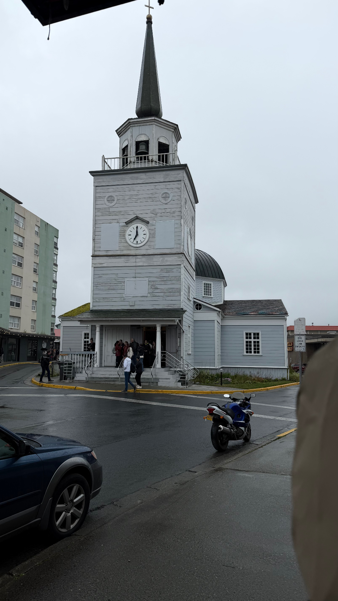 St. Michael's Orthodox Cathedral in Sitka, a white wooden church with a clock tower, bell tower and dark onion dome, on a rainy street corner