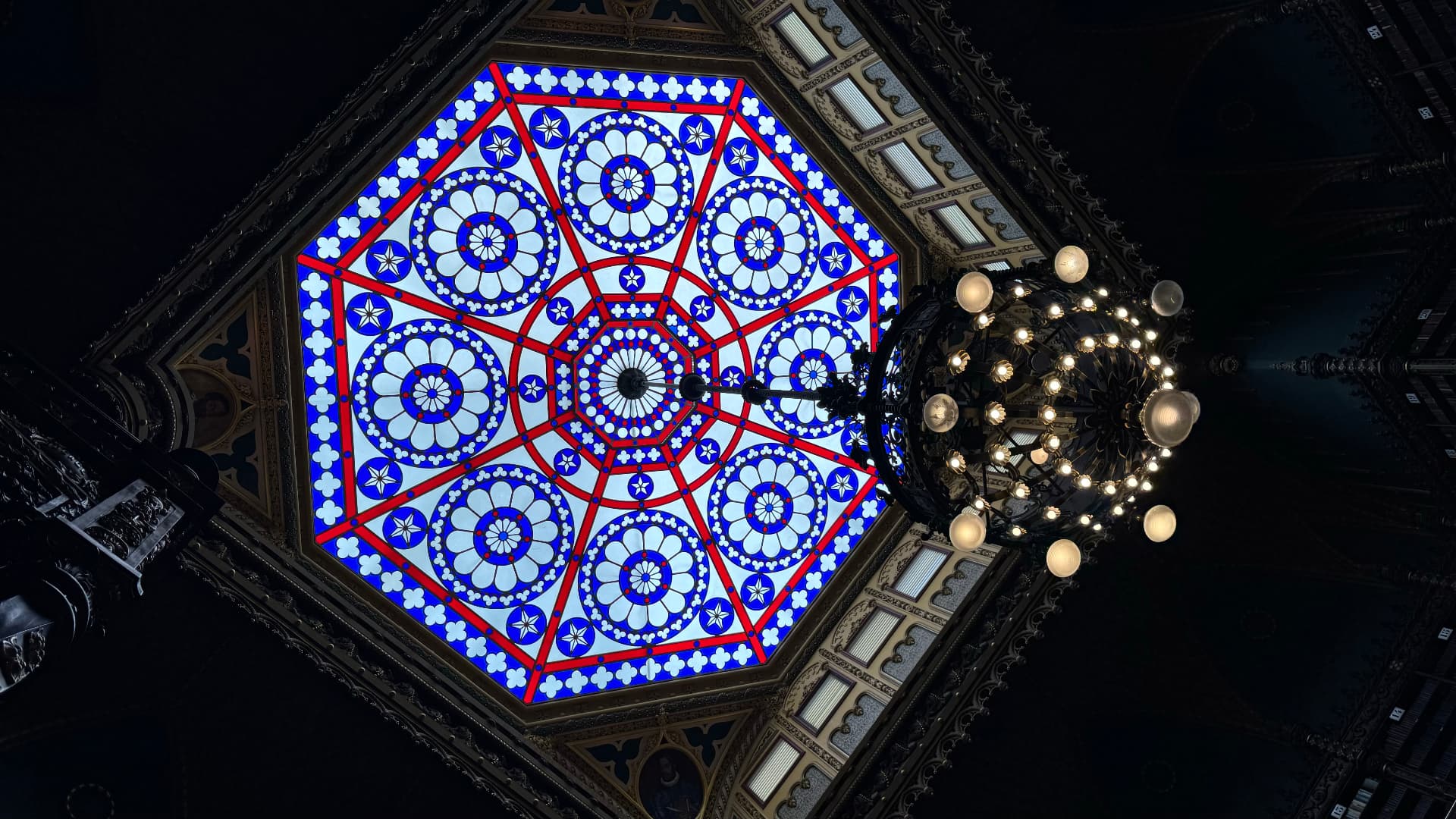 Stained-glass skylight and chandelier glowing against the dark library interior