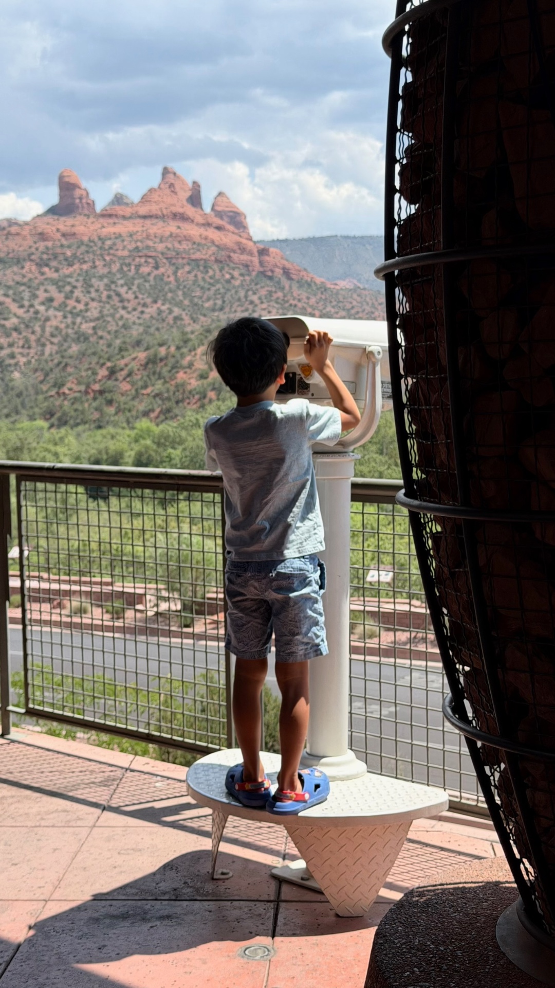 Kayden on a step stool looking through a viewing scope at the red rocks