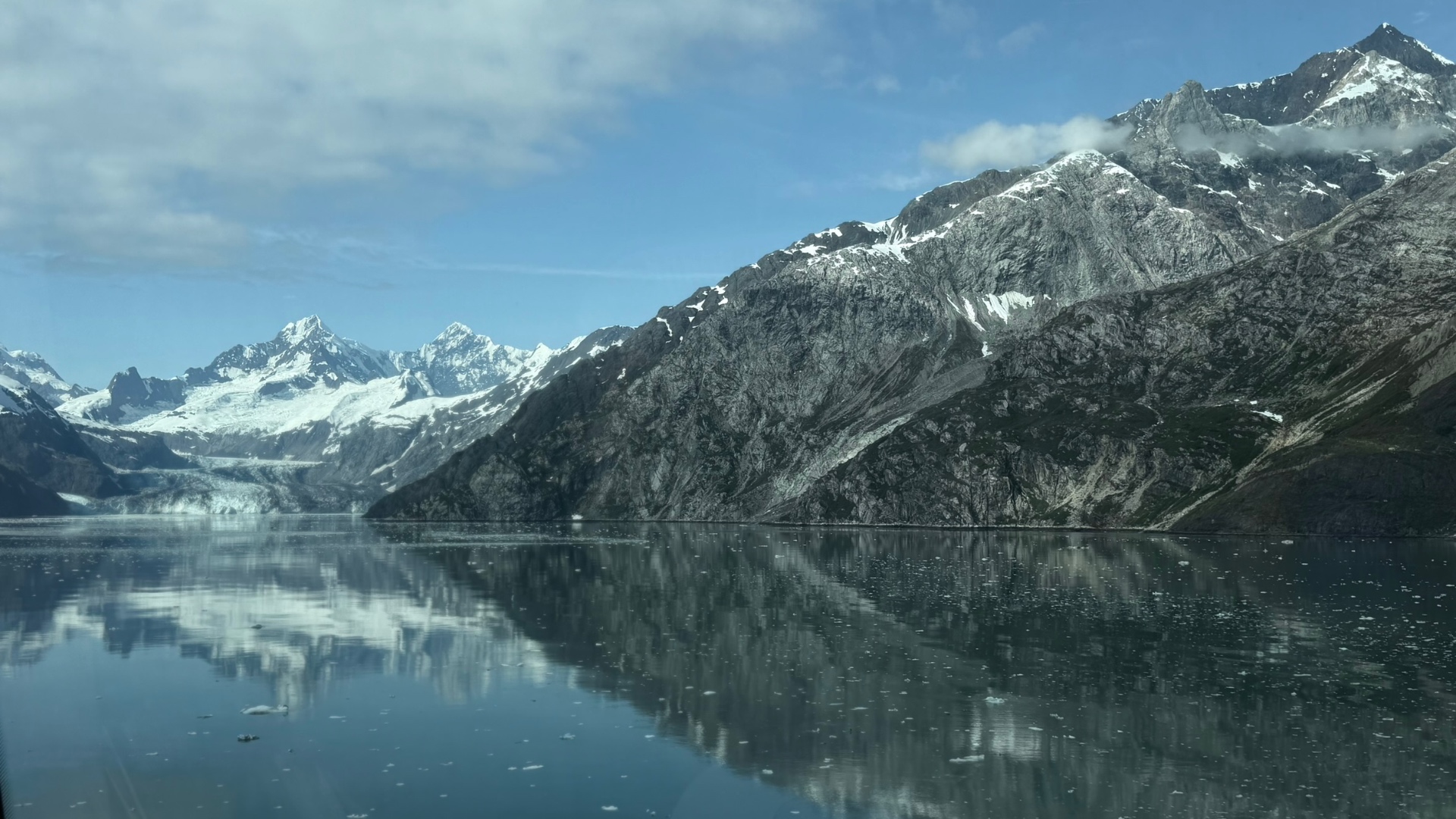 Snow-covered mountain peaks and a glacier reflected in the still water of Glacier Bay