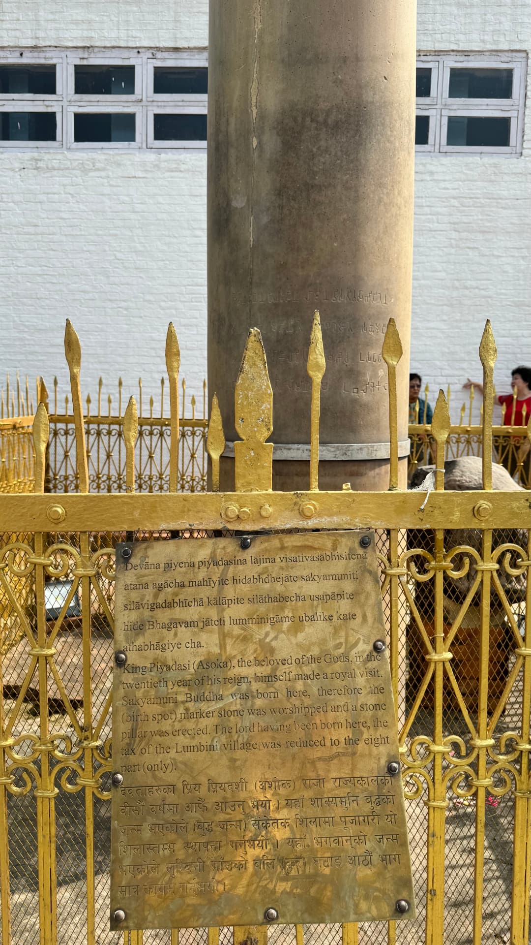 The Ashoka pillar and its information plaque behind a golden railing. — Lumbini, Nepal.