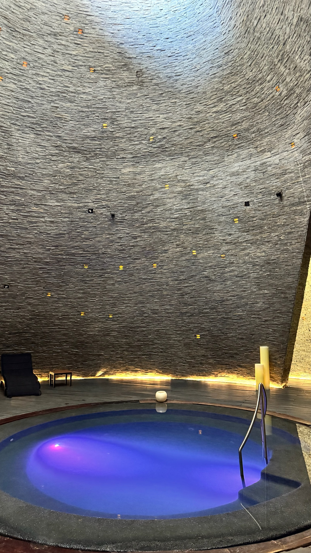 Circular spa pool glowing blue beneath a tall stone chamber