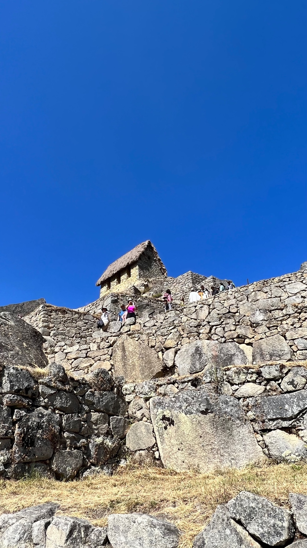 Steep stone terraces and a thatched guardhouse beneath a deep blue sky