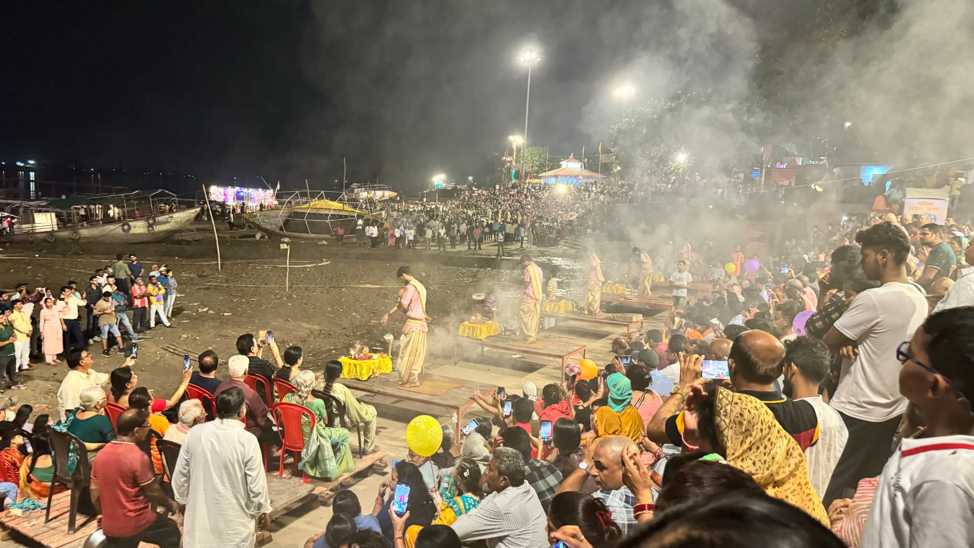 Crowds gather for an evening riverside ceremony amid light and smoke. — Varanasi, Uttar Pradesh, India.