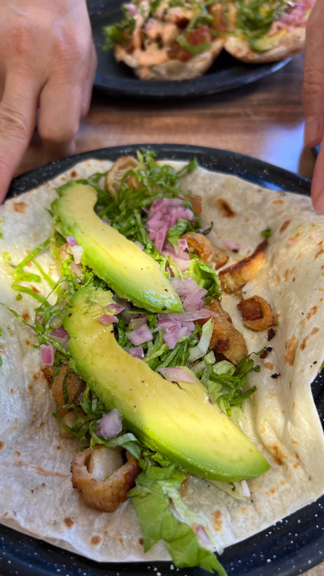 Taco filled with grilled seafood, avocado, onion, and greens