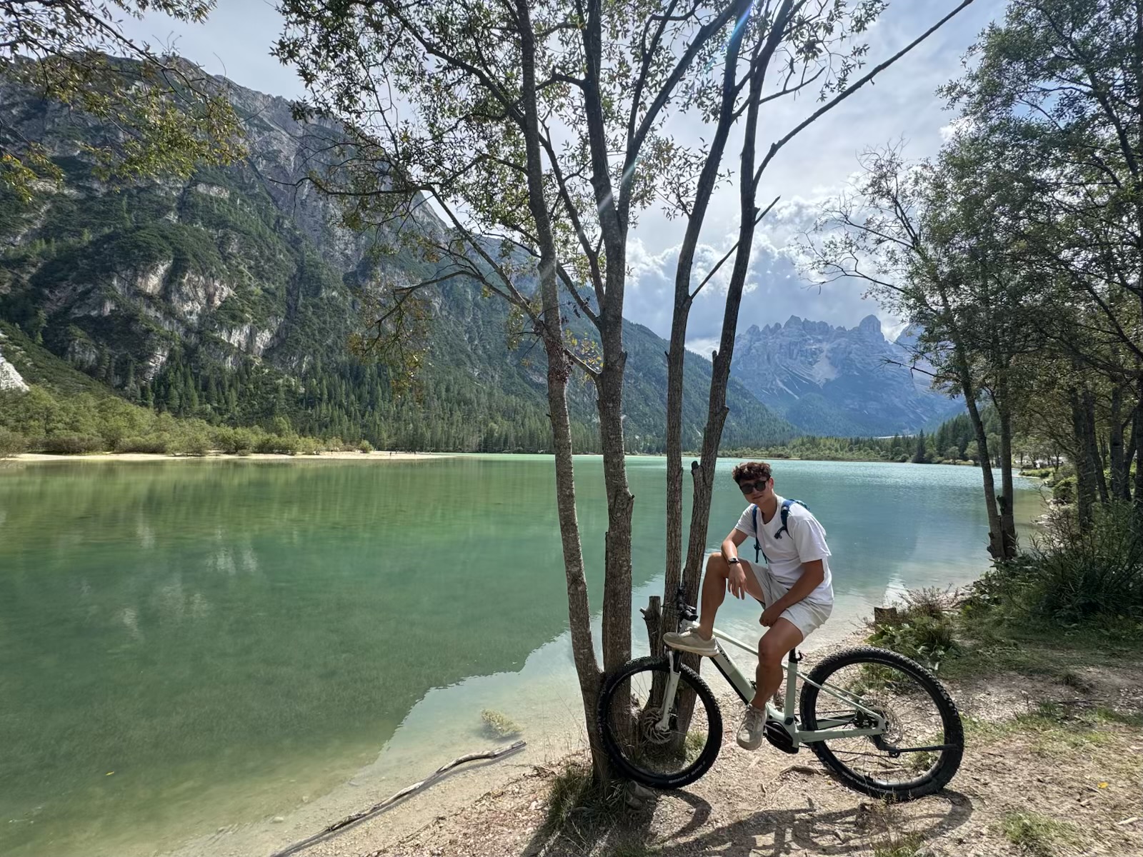 Kayden posing with a mountain bike beneath trees beside a clear green lake