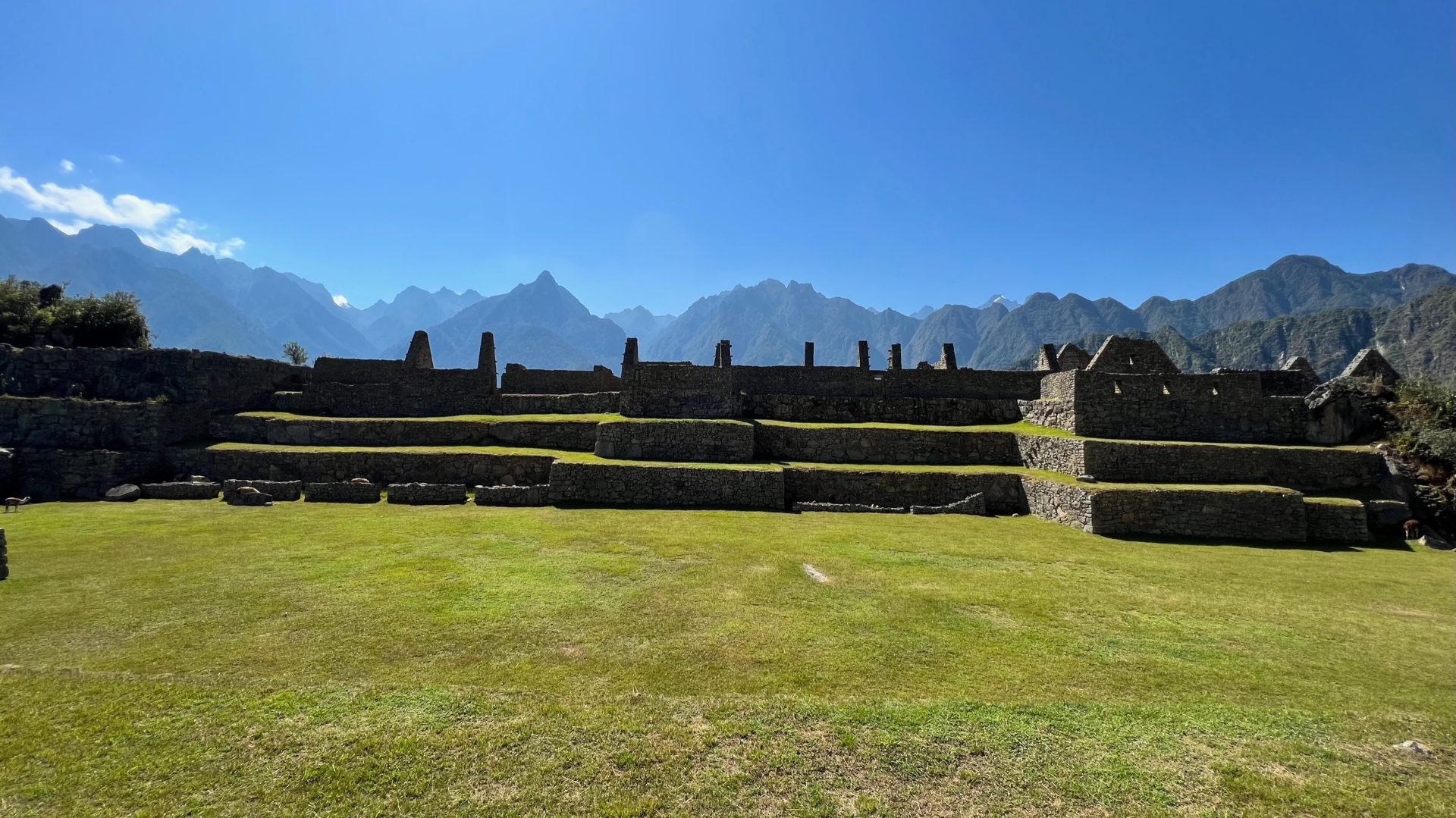 Green ceremonial lawn and stone terraces beneath a wide Andean skyline