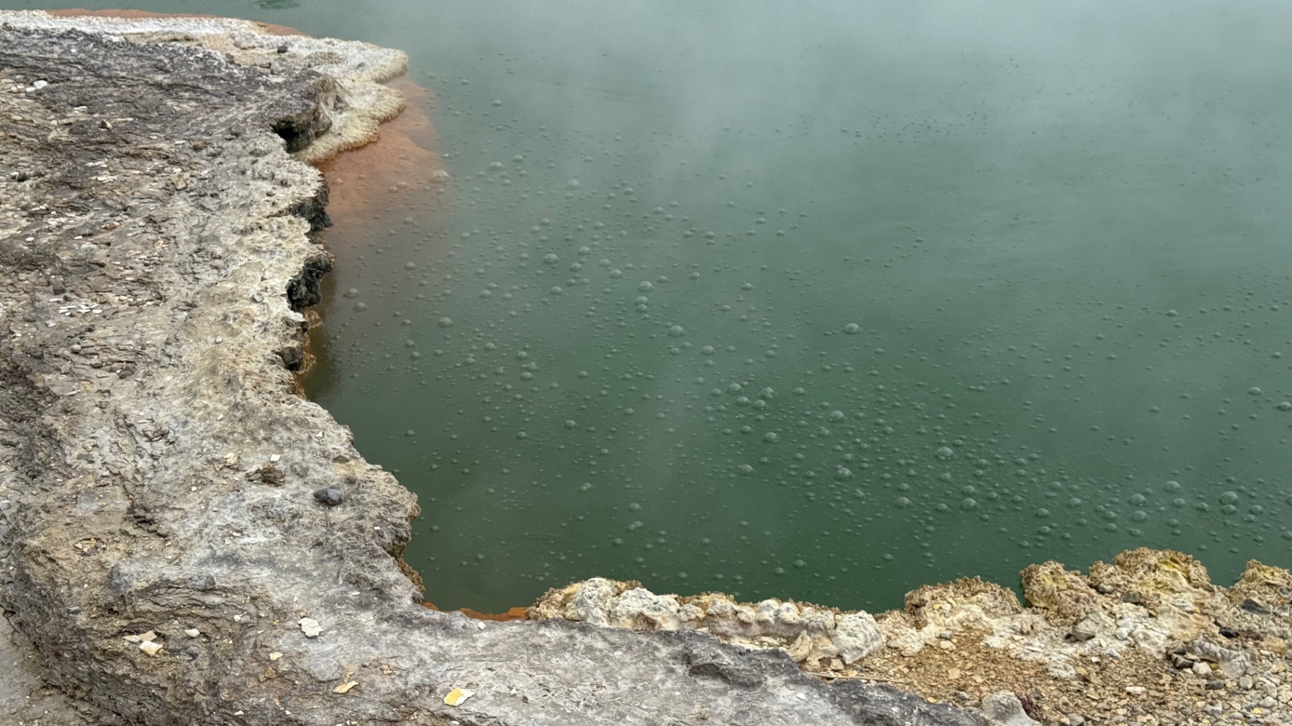 Bubbles rising through the jade water of a hot spring beside a crusted mineral edge