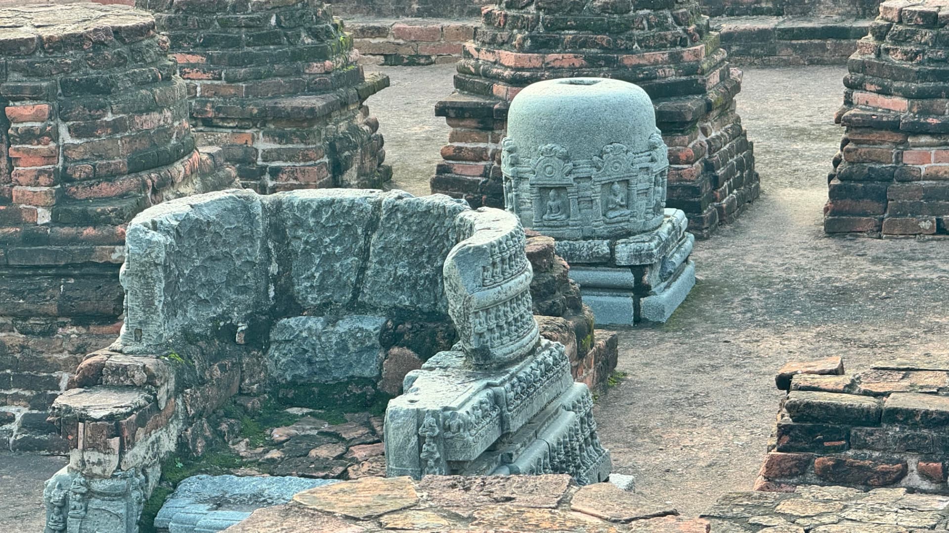 Carved stone fragments stand among the ancient brick remains. — Nalanda, Bihar, India · Patna chapter.